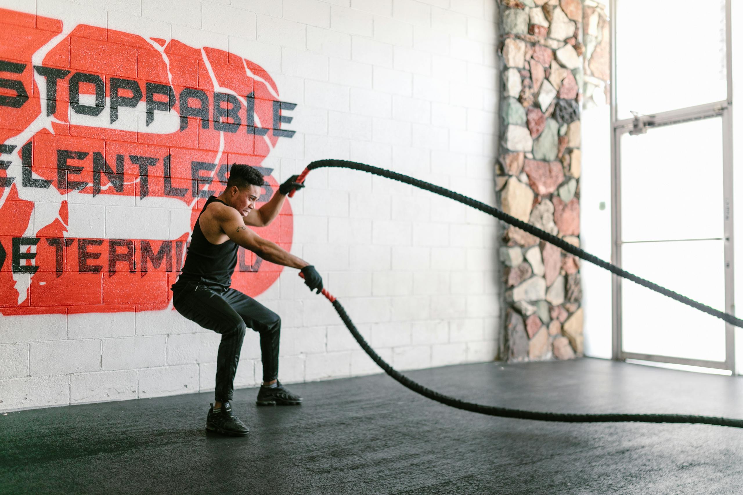 Athletic man training with battle ropes in a gym with motivational wall art.
